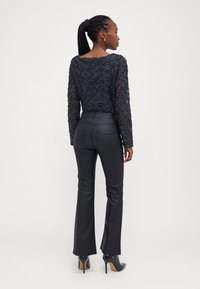 Zwarte blouse met lange mouwen en een gestructureerd kraalpatroon, gecombineerd met zwarte flared broek. Afgemaakt met hoge hakken met een puntige neus.