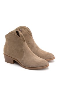 Para beżowych zamszowych botków za kostkę z niskimi blokowymi obcasami i zamkami błyskawicznymi po bokach, prezentowanych na białym tle.