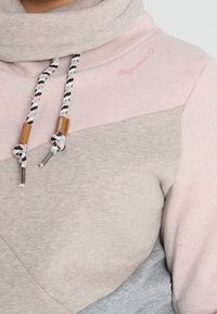 Sudadera con capucha que presenta un diseño bicolor en rosa claro y gris. El material es suave, con cordón y detalles de madera para ajustar.