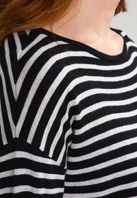 Pull rayé noir et blanc avec une texture douce, un col large et une coupe décontractée. Les rayures varient en largeur sur le tissu.