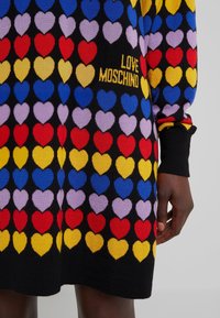 Robe en maille avec motif de cœurs multicolores en rangées, manches retroussées, et texte "LOVE MOSCHINO" en jaune sur fond noir.