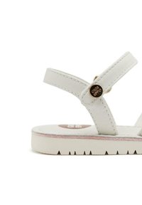 Sandal in pelle bianca con due cinturini, decorata con accenti metallici e una spessa suola in gomma. Presenta cuciture a vista e un bordo rosa.