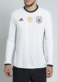 Vit långärmad fotbollsjacka med svarta detaljer, FIFA-märke och Tyska fotbollsförbundets emblem. Tillverkad av ventilerande material.