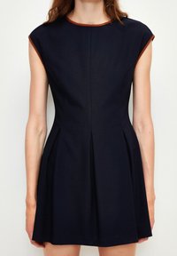 Marinblå klänning med korta ärmar, rundad halsringning, bruna detaljer, figurnära midja och utsvängd kjol med veck bak. Slät tygstruktur.