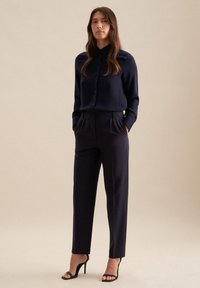 Navy-blaues Hemd mit langen Ärmeln, kombiniert mit hoch-taillierten, maßgeschneiderten navy-blauen Hosen und schwarzen Absatzsandalen. Glatte Stoffbeschaffenheit.