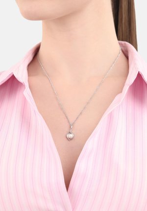 Collana d'argento con un design intrecciato e un piccolo pendente di perla bianca, indossata su una blusa a righe rosa chiaro.