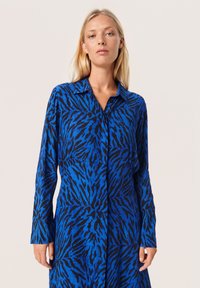 Rochie cămașă albastră cu un model de dungi negre de tigru. Dispune de un guler și mâneci lungi, realizată dintr-un material neted și ușor.