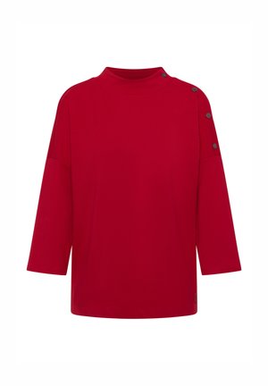 Chemise surdimensionnée rouge avec un col haut, des manches trois-quarts et des boutons décoratifs noirs sur l'épaule gauche. Texture de tissu lisse.