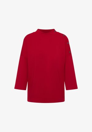 Červená oversize ko shirt s vysokým výstřihem, tříčtvrtečními rukávy a dekorativními černými knoflíky na levém rameni. Hladká textura látky.
