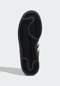Black rubber shoe sole with a zigzag tread pattern. Features smooth textured areas and a logo on the bottom edge.