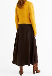 Pull en tricot jaune associé à une longue jupe marron foncé et des bottes en cuir marron à hauteur du genou, à motif. Texture lisse et silhouette décontractée.