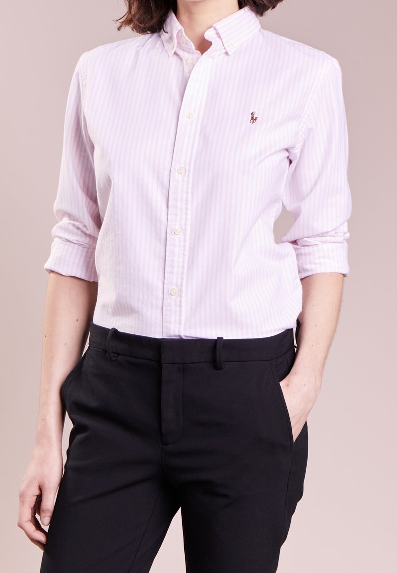 Ljusrosa randig skjorta med button-down krage, försedd med en liten broderad logotyp. Bärs tillsammans med svarta skräddarsydda byxor som visar en slät textur.