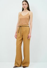Bruine spaghetti-top gecombineerd met hoge, wijdvallende mosterdkleurige broek met een gevlochten riem. Zachte textuur en minimale details.