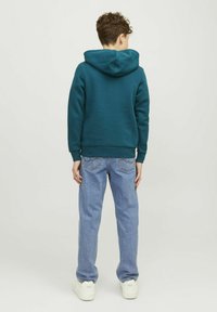 Felpa verde acqua con una finitura testurizzata, dotata di cappuccio e polsini a costine, abbinata a jeans blu chiaro e sneakers bianche.