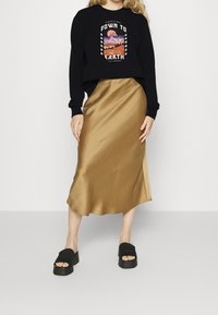 Sudadera negra con estampado gráfico, combinada con una falda larga de satén dorado. La modelo lleva sandalias de plataforma negras. Diseño simple y moderno.