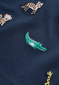 Tissu bleu marine avec des animaux de dessin animé brodés, y compris un tigre, un crocodile, une girafe et un singe.