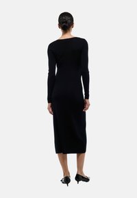 Robe noire à manches longues en matériau tricoté texturé, avec un design ajusté qui tombe au milieu du mollet. Assortie à des chaussures noires à talons hauts.