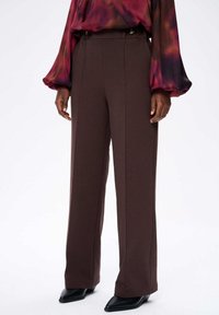 Bruine wijde broek van zachte stof, met een hoge tailleband, verticale naden en knoopaccenten aan de voorkant. Gecombineerd met een losvallende, multikleurige top.