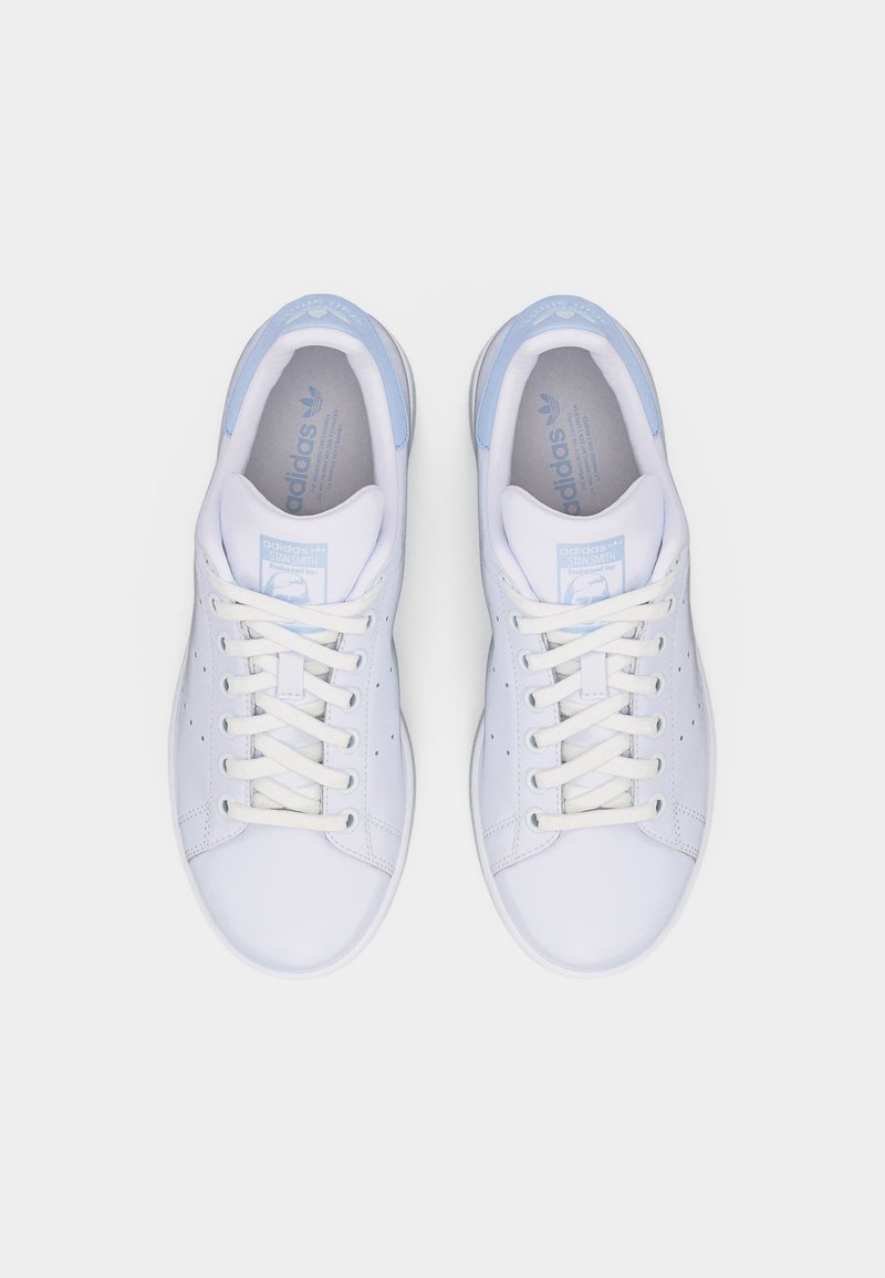 Par hvide Adidas Stan Smith sneakers med lyseblå hælkapsler og snørebånd, set ovenfra på en hvid baggrund.
