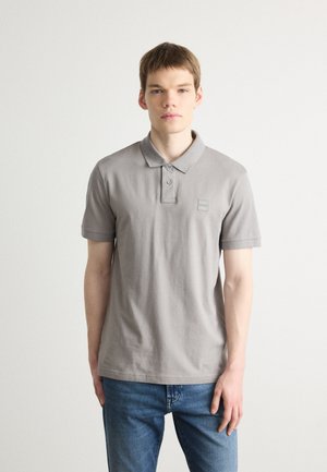 Polo gris en coton, avec un col à boutons, des manches courtes et un patch logo carré sur la poitrine. Assorti à un jean en denim.