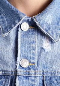 Giacca di jeans azzurro chiaro con colletto, caratterizzata da bottoni metallici e dettagli consumati, che mette in risalto una texture intrecciata e cuciture visibili.