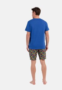 Blå bomulds T-shirt med korte ærmer, parret med farverige shorts med sommerfuglemotiv, der viser en blanding af lyse farver på en mørk baggrund.