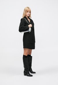 Černé oversized sakašaty, černé kožené kozačky ke kolenům s blokovým podpatkem, stříbrná kovová kabelka, hladká tkanina, jednobarevný zapínací design.