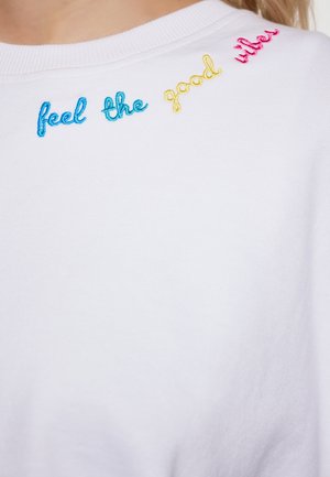 Witte sweatshirt met geborduurde tekst in blauw, geel en roze met de tekst "voel de positieve vibes." Zachte stof met een ontwerp met ronde hals.