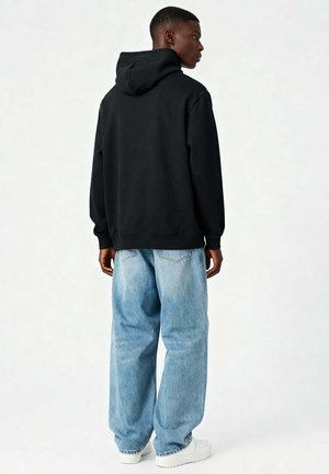 Haut noir à capuche, avec une grande capuche, coupe décontractée, poignets côtelés, associé à un jean baggy bleu clair et des baskets blanches. Texture en coton lisse.