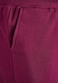 Burgundy sweatpants with a soft texture, featuring a side pocket and elastic waistband for comfort and fit.