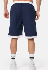 Navy shorts with white waistband and hem, front pockets, and a lightweight fabric. Worn with white socks featuring two black stripes.
