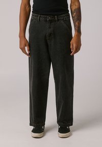 Black denim pants with a relaxed fit, featuring a zipper fly, five pockets, and subtle stitching details. Worn with black shoes.