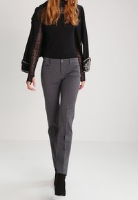 Grå skräddarsydda byxor med en slät textur, med en figurnära passform, framfickor och knappstängning. Stylade med en svart topp och högklackade stövlar.