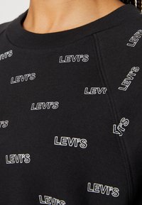 Felpa nera con loghi "LEVI'S" bianchi sparsi, scollo rotondo e tessuto testurizzato con una finitura morbida.