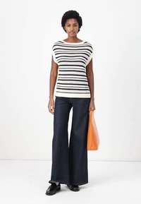 Strikket topp med svart-hvite striper, bred halslinning; parret med mørke, vide jeans og en oransje veske. Jevn tekstur og moderne design.