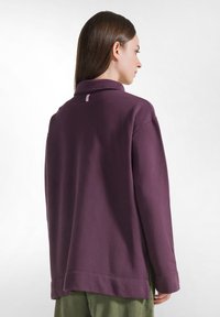 Lila Pullover mit langen Ärmeln und hohem Kragen, lockerer Schnitt und seitlichen Schlitzen. Verfügt über ein kleines Logotag im Nacken hinten.