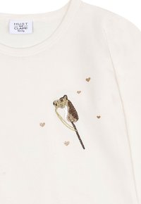 Cremfarbendes Babyshirt mit besticktem braun-weißen Schaukelpferd und kleinen goldenen Herzen im Brustbereich.