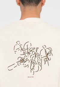Rückseite eines weißen Shirts mit einer braunen Linienzeichnung einer fünfköpfigen Jazzband, die verschiedene Instrumente spielt, und dem Wort "SELECTED" darunter.