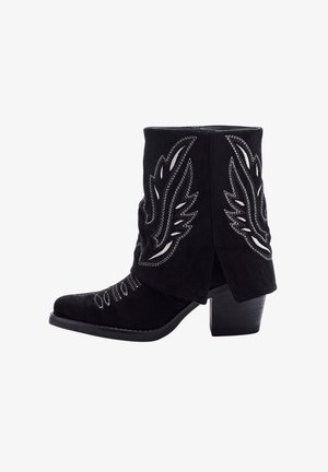 Botín negro de ante con costuras plateadas decorativas y diseño en forma de alas, que presenta un tacón cuadrado y punta afilada.