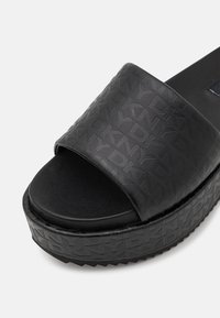 Sandale à plateforme noire à enfiler avec motif logo DKNY en relief sur la bride et la semelle, design à bout ouvert et semelle inférieure texturée pour une meilleure adhérence.