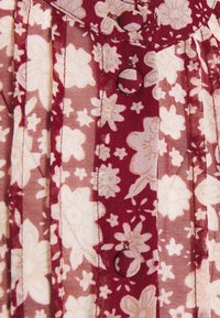 Tissu de robe florale avec un fond bordeaux orné de fleurs crème. Comprend des boutons et des plis, mettant en valeur une texture douce.