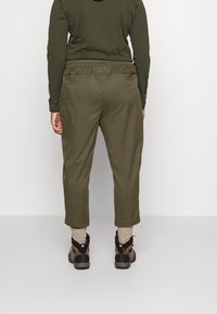 Pantalons verts olive avec taille élastique, coupe décontractée, longueur cropped et poches latérales ; associés à des bottes marron et des chaussettes en grosse maille.