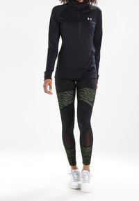 Czarna, długosłhawa odzież sportowa z kołnierzykiem zapinanym na zamek, w połączeniu z dopasowanymi legginsami z czarno-oliwkowymi wzorami w paski tygrysa. Białe trampki.