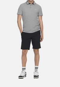 Graues Poloshirt mit schwarzem Kragen und Besatz, kombiniert mit navyblauen Shorts. Getragen mit schwarz-weißen Turnschuhen und gestreiften Socken.