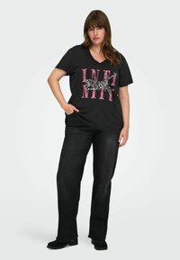 Zwarte V-hals t-shirt met roze "INFINITY" graphic en een gestreept kattenontwerp; gecombineerd met donkere spijkerbroeken en zwarte schoenen. Eenvoudige, casual look.