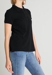 Polo noir en coton, avec col, fermeture à boutons et manches courtes. Associé à un jean bleu pour un look décontracté.