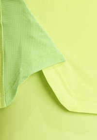 Lichtgroene sportstof met een gestructureerd patroon, voorzien van een gladde naaddetail en contrasterende vlakken in een effen kleur.