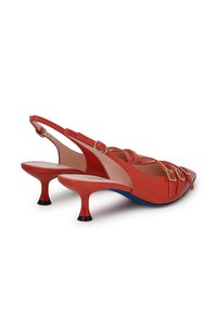 Scarpe slingback in vernice rossa con punte appuntite, dettagli decorativi con fibbie e tacco in contrasto blu e nero. Texture liscia.