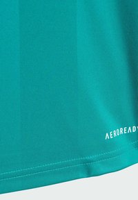 Zbliżenie na turkusową tkaninę z podwójnym szwem oraz małym białym logo "AEROREADY" w pobliżu dolnej krawędzi.