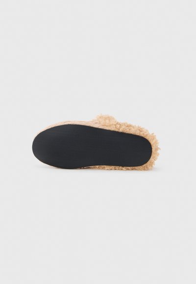 Chausson beige clair doublé de fourrure avec une tige texturée, une forme incurvée et une semelle extérieure en caoutchouc noir lisse pour l'adhérence.